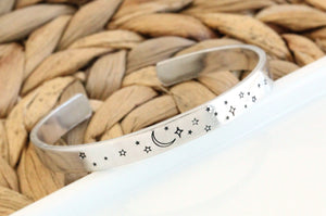Silver-colored aluminum cuff bracelet featuring a crescent moon and an array of various stars